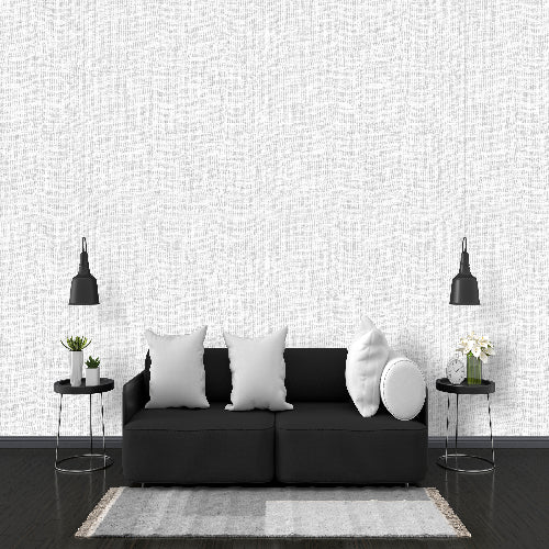 Modern living room with a black sofa, white pillows, and decorative items against a white textured wall.