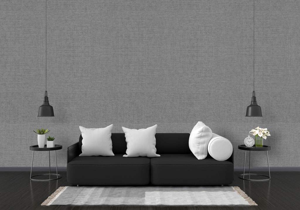 Modern living room with a black sofa, white pillows, and decorative items against a gray wall.