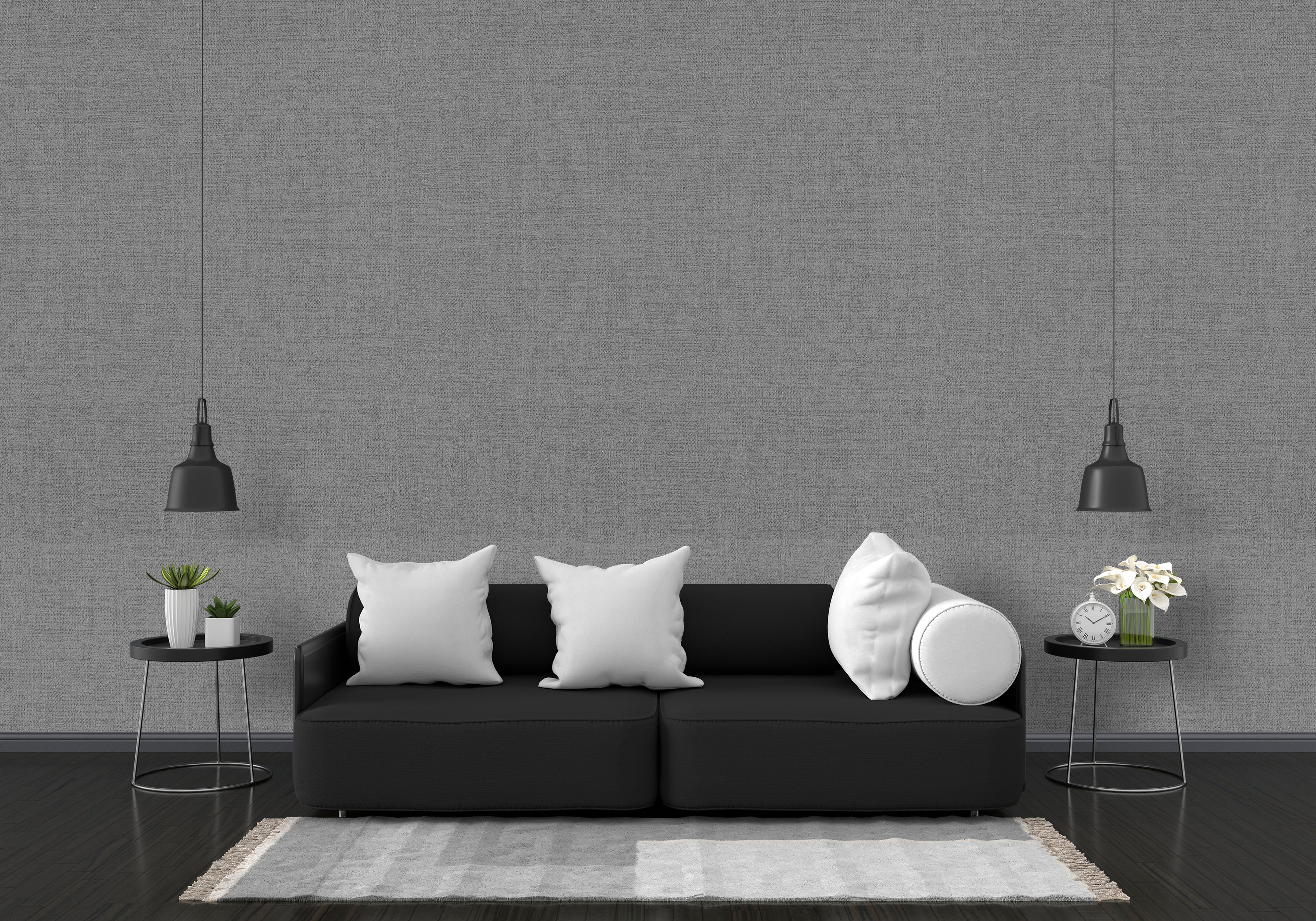 Modern living room with a black sofa, white pillows, and decorative items against a gray wall.