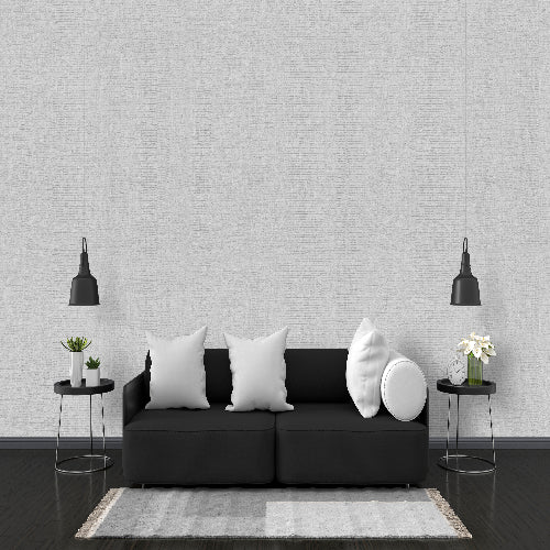 Modern living room with a black sofa, white pillows, and decorative items against a gray wall.