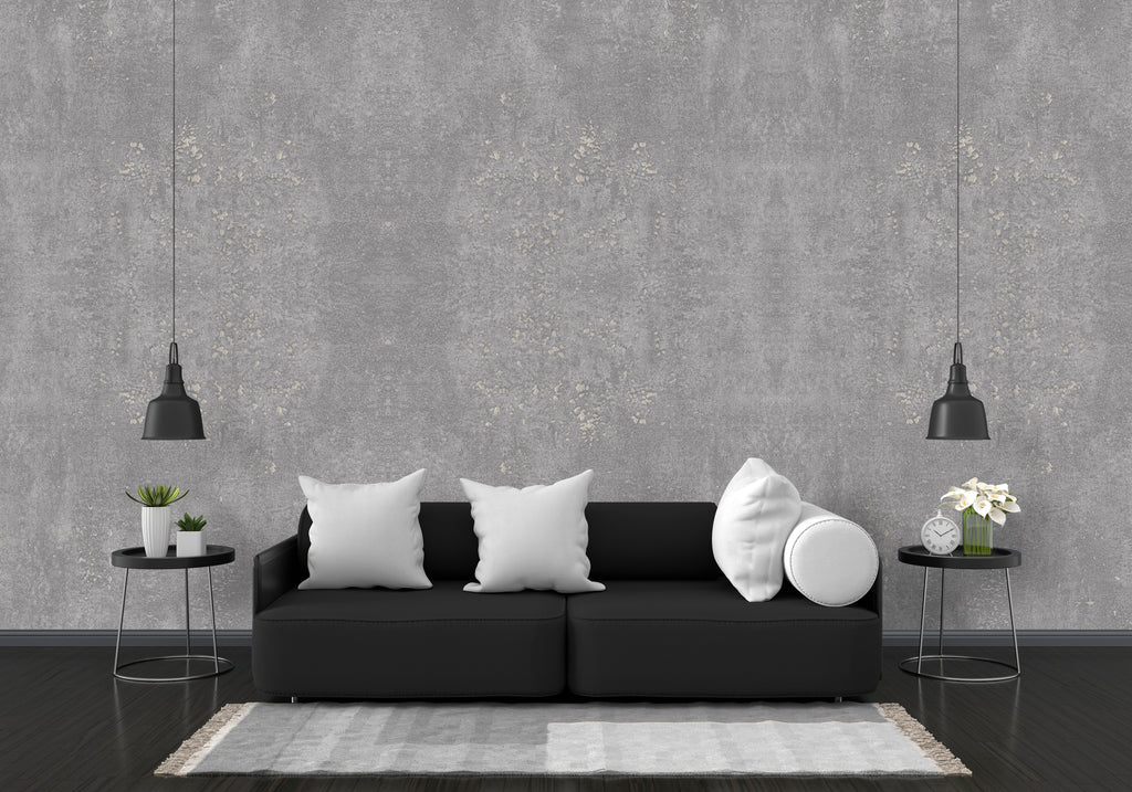 Modern living room with a black sofa, white pillows, and decorative items against a gray concrete wall.